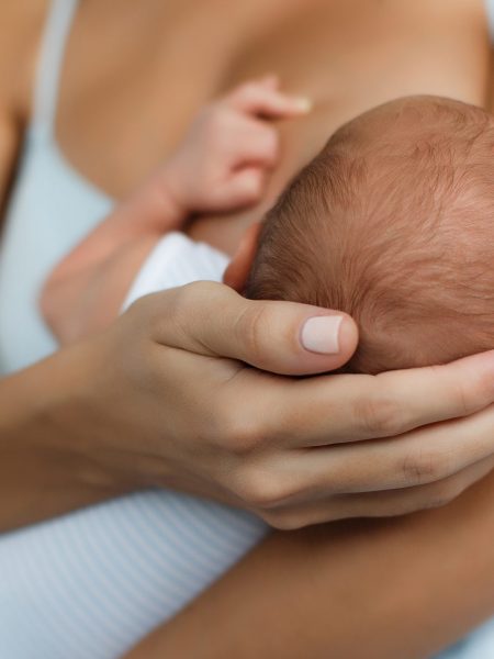 Happy young mother, sitting in the bedroom with her newborn son in her arms,gently supports the child's head with your hand, feeds the baby's chest,the boy greedily sucks her mother's breast